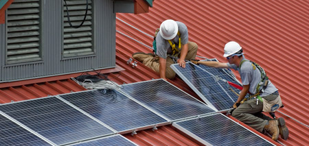 Two workers install solar panels on a red roof